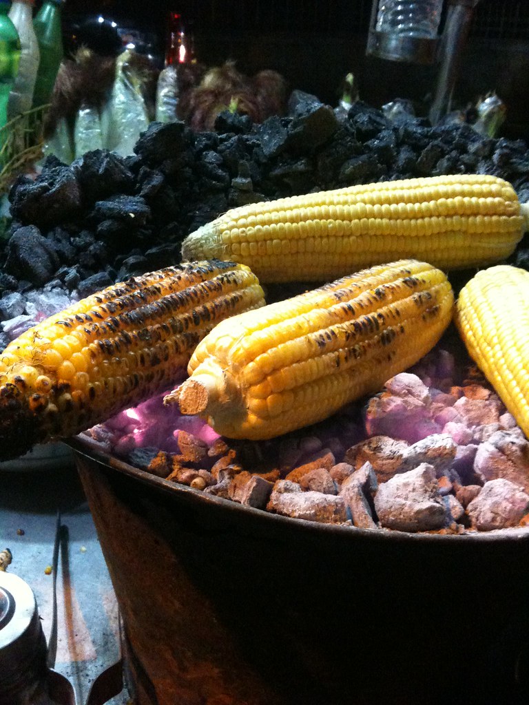 Sweet corn cobs roasting over glowing charcoal embers